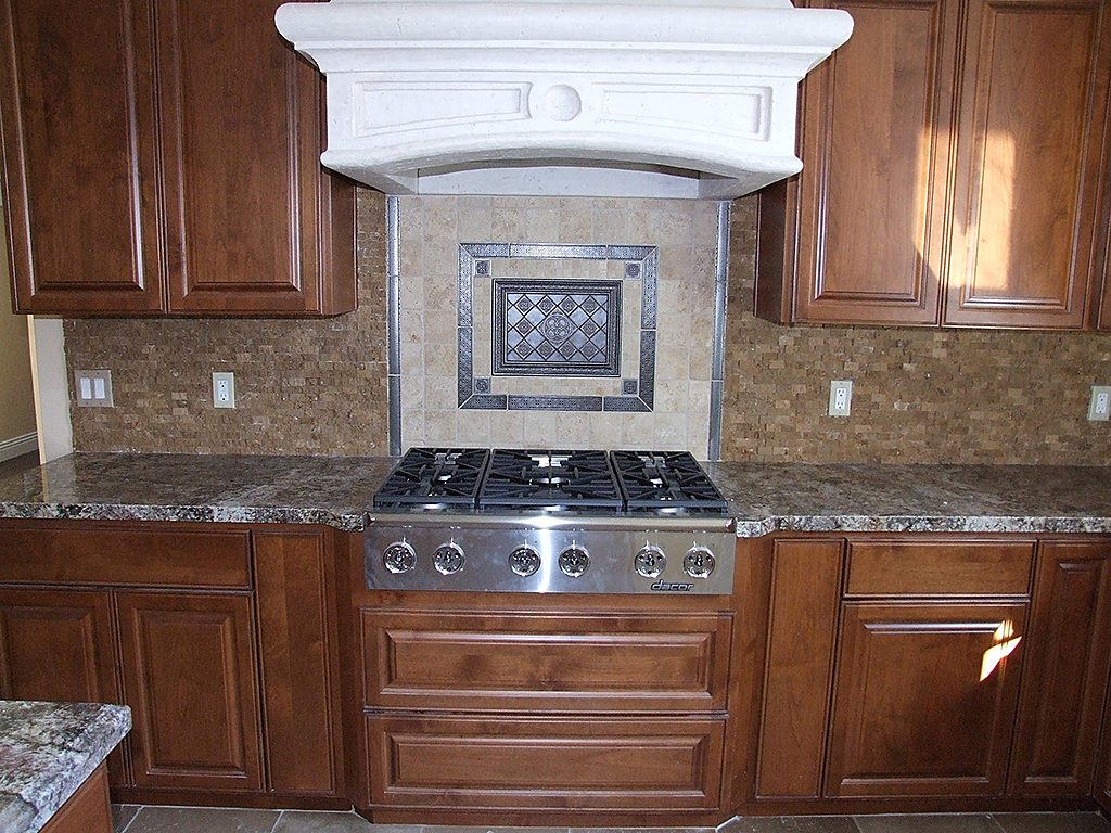 Kitchen stone countertops and rought stone tile backsplash. Detailed tiling with insets above embedded stove.
